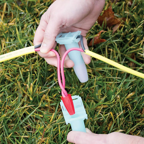 Hands connecting wires with Direct Burial Wire Connector DryConn DIY Friendly Blue Waterproof Sealant in garden setup.