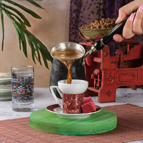 Hand Hammered Copper Turkish Coffee Pot 12 Oz With Wooden Handle being used to pour coffee into a cup on a table
