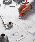 Engineer using red pencil on technical drawing with mechanical parts on table.