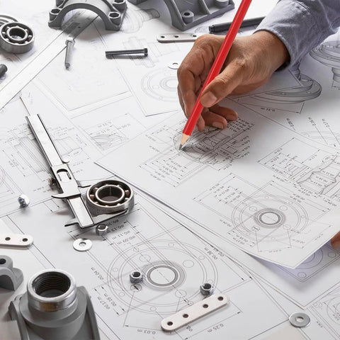 Engineer using red pencil on technical drawing with mechanical parts on table.