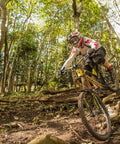 Mountain biker navigating trail in wooded area with dappled sunlight filtering through trees.
