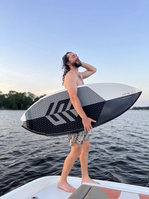 A person holding the Mondo 5 Foot 2 Inch Wakesurf Board with EVA Padding Thruster Fin Design DuraFloat Core Ultra Light Build on a boat.