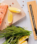 Wireless Smart Meat Thermometer for Oven, Grill, Kitchen, BBQ and Smoker with Bluetooth and WiFi Connectivity next to salmon and herbs