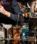 A bar setting with a Six Size Low Form Glass Beaker Set With Printed Graduation For Accurate Measurement Includes 25Ml 50Ml 100Ml 250Ml 500Ml 1000Ml 3.3 Borosilicate Glass Lab Beakers With Large Markings used for cocktails.