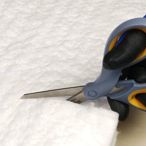 Ceramic fiber insulation blanket, white, being cut with blue-handled scissors.