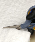 Ceramic fiber insulation sheet, white, being cut with blue-handled scissors