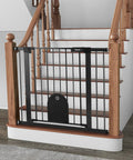 Wide Auto Close Baby Gate With Cat Door For Easy Walk Through Adjustable 29.7 To 40.6 Inches Pressure Mounted Or Hardware Mounted Durable Pet Gate For Stairs And Doorways Black installed at the bottom of a wooden staircase