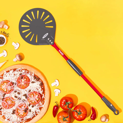 TKC 9-inch perforated aluminum pizza peel with long red handle, front view on yellow background
