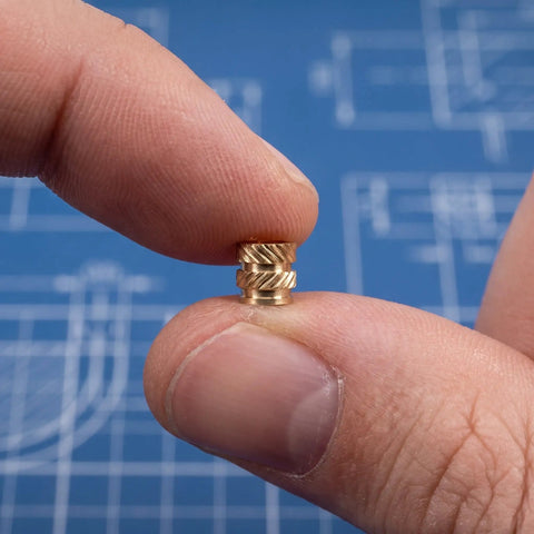 Close-up of Premium 48Pcs Brass M4 Heat Set Threaded Inserts For 3D Printing with knurled design held between fingers.