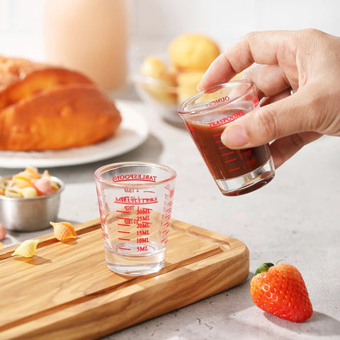 Hand using Two Pack Shot Glass Measuring Cup Set With Thick Base, Multi Unit Liquid Measuring Cup For Espresso And Drinks, Four Measuring Scales Include 1 OZ, 2 TBS, 6 TSP, 30 ML For Precise Pouring