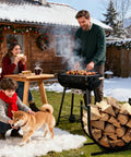 17 Inch Heavy Duty Firewood Rack Holder for Indoor and Outdoor Use next to a family enjoying a barbecue in a snowy backyard.