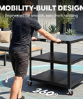 Person maneuvering Heavy Duty Outdoor Pizza Oven Table 36 By 24 Inches With Locking Wheels 304 Stainless Steel Worktop Built Tough Three Shelf Prep Unit For Deck Patio BBQ And Parties on patio.