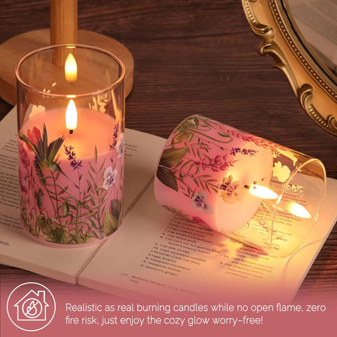 Pink Hummingbird Glass Flameless Candles Set Of 3 With Remote Control Flickering LED Pillar Candles Battery Operated Real Wax In Glass For Cozy Vibes Spring Home Shelf Decor. One candle lit on book.