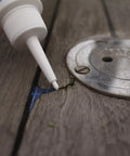 Applying Creeping Crack Cure 8oz Sealant For Hairline Gaps And Cracks on wooden surface near metal fixture.