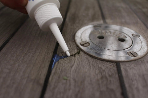 Applying Creeping Crack Cure 8oz Sealant For Hairline Gaps And Cracks on wooden surface near metal fixture.