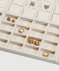 Totally Sweet Beige Linen Jewelry Display Tray With Sixteen Grid Slots For Rings Necklaces And Bracelets Ultra Soft Fabric Organizer showcasing various gold jewelry pieces.