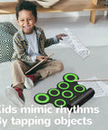 Child playing Portable Electronic Drum Set For Practice And Performance With Snare Toms Crash Ride Hi Hat Pads And Dual Foot Pedals Roll Up Drum Kit 5 Timbres 8 Demo Songs And 3 Rhythms For Beginners And Kids, smiling with drumsticks.