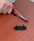 Hand holding screwdriver next to 12 Sets Black Stainless Steel Straight Brackets With Screws For Beds And Shelves on wood surface.
