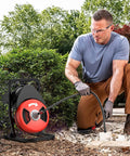 Rugged Heavy Duty 50 Foot Electric Drain Snake And Sewer Auger Toolkit With Solid Half Inch Steel Cable For Snagging Gunk And Ripping Tree Roots In Two To Four Inch Pipes Powered By Badass 450 Watt Motor used outdoors by a man clearing a blockage.