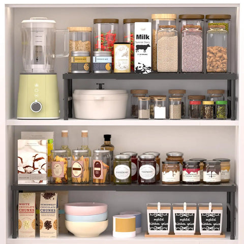 Hella Adjustable And Stackable Kitchen Cabinet Organizer displaying jars and spices on a metal pantry shelf in a kitchen cupboard.