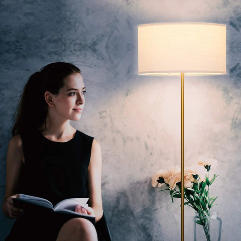 Quinn LED Floor Lamp With Drum Shade Sleek Modern Standing Light next to reading woman in living room, brass gold finish