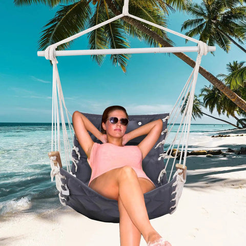 Woman lounging in Cozy Hammock Chair Swing With Wooden Armrests, Sturdy Steel Spreader Bar, Plush Back Pillow on a beach.