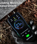 Gloved hand holding a digital wood moisture meter with pin probes for firewood, drywall, and lumber. Screen displays building moisture level.