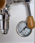 Close-up of Mini Cellini Espresso Machine with steam wand and pressure gauge, featuring white paneling and chrome accents.