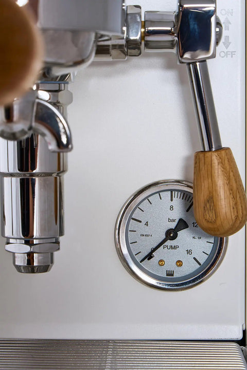 Close-up of Mini Cellini Espresso Machine with steam wand and pressure gauge, featuring white paneling and chrome accents.
