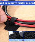 Close-up of a black self-adhesive hook-and-loop cable tie managing red and black cables on a desk surface