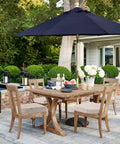 Patio dining set with wooden table and chairs, blue umbrella, and garden background.