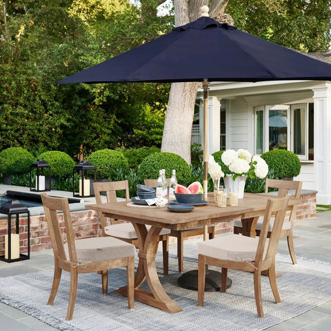 Patio dining set with wooden table and chairs, blue umbrella, and garden background.