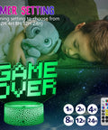 Child sleeping with green 'Game Over' 3D illusion gamer night light, remote control and timer settings shown.