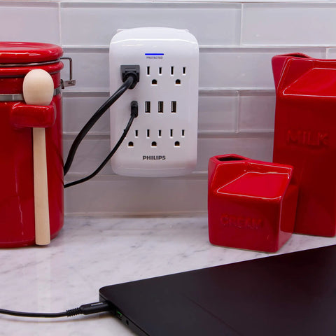 Six Outlet Surge Protector Power Strip With Four USB Ports Dual Pack Charging Station 900 Joules Of Surge Protection 3 Prong Grounded Design Wall Mount Friendly ETL Listed White mounted on wall.