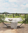 Two Person Outdoor Hammock With 12 Ft Steel Stand For Easy Setup No Trees Needed Portable Beach Patio Garden Chill Vibes 475 Lb Capacity Breathable Cotton Rope And Quilted Pad Weather Resistant Easy Fold Storage Case Included shown on a balcony.