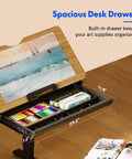Flexispot Electric Drafting Table With Adjustable Height And Tilting Top 47.2 By 23.6 Inches Extendable Workstation with open storage drawer displaying art supplies.