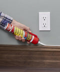 Flex Caulk white sealant tube with red cap being applied to wood baseboard beside wall outlet