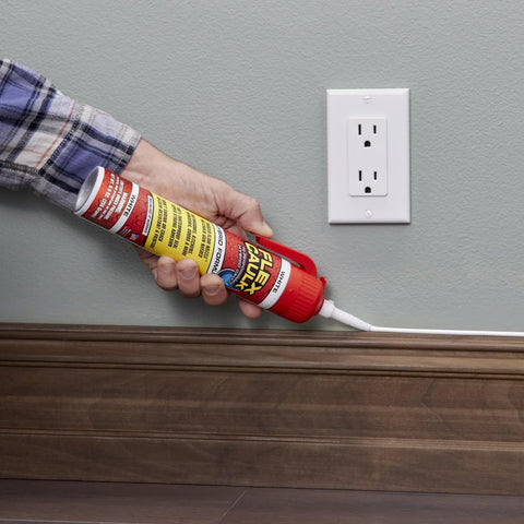 Flex Caulk white sealant tube with red cap being applied to wood baseboard beside wall outlet