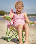 Child seated on Kid Sized Butterfly Back Folding Chair With Built In Cup Holder In Armrest, enjoying a sunny beach day.