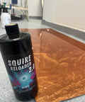Squire Two Zero Reloaded Pro Grade Sealer For Concrete Epoxy Natural Stone Vct Lvt Lvp Tile And Grout Substrates With Gloss Finish One Quart Coverage Up To 250 Sqft with glossy copper surface in background.