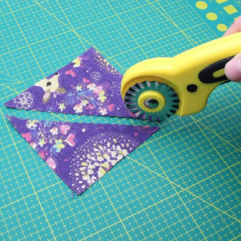 45mm Wavy Rotary Cutter With 10 Piece Pinking Circular Refill Blades cutting patterned fabric on a green mat.