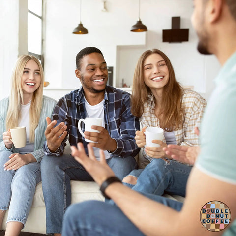 Group of four friends sitting on a sofa enjoying coffee, each holding a mug, in a cozy living room setting with warm lighting.