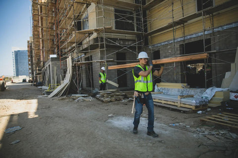 Mens High-Vis Mesh Vest With Zip-Front And Neon Lime Shade To Stay Fresh While Working Hard worn by a worker carrying lumber on a construction site.