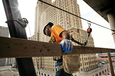 Construction worker wearing Original 1994 Crinkle Grip Work Gloves With Natural Latex Palm, Blue, Small, with city skyline.