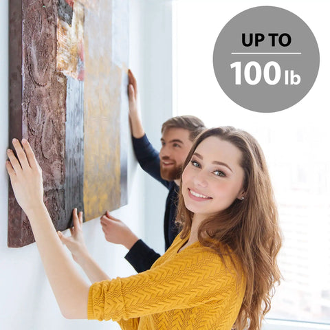 Two people hanging a painting using Pro Grade All In One Picture Hanging Kit With Stainless Steel Wire D Rings Hooks Screws And Level