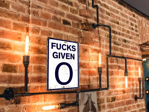 Heavy Duty Badass Zero Given Metal Sign For Man Cave Garage Wall Decor Rust Proof Vintage Bar Art 12x8 Inch on exposed brick wall.