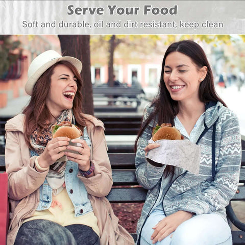 Two women enjoying burgers wrapped in insulated foil wrap sheets, demonstrating greaseproof and leakproof qualities, in a park setting.