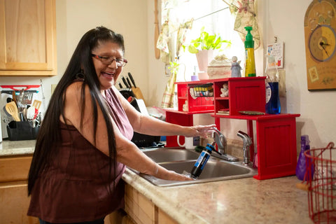 Woman using Tap Water Filtration System With 0.1 Micron Inline Filter, Fits Faucets And Hose Bibs, Keeps Camp Water Fresh For Camping, RVs, Emergencies And Travel, Filters Up To 500 Gallons Per Day, Blue in kitchen sink.