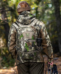 Person wearing Camo G2 25L Hunting Backpack With Waterproof Rain Cover And Tough 600D Daypack For Bow Rifle Gun in forest
