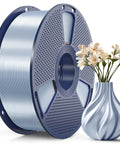 Blue spool of silk-silver PLA filament for 3D printers, 1.75mm, beside a decorative vase